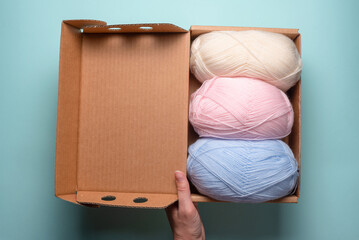 Balls of woolen thread in the cardboard box parcel in the female hands flat lay background. Free shipping of knitting accessories.