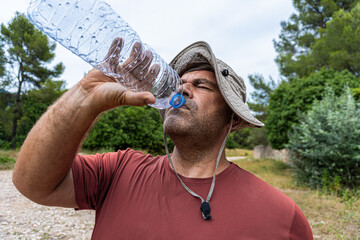 Caucasian hiker man wearing a hat and very sweaty, finishing water from a plastic bottle, on a very hot day. 