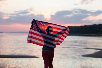 a woman with an American flag on the ocean at sunset. Independence Day. The United States celebrates July 4.
