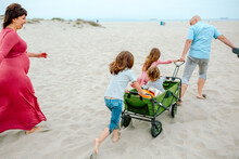 Family Pulling Green Wagon Across Sand