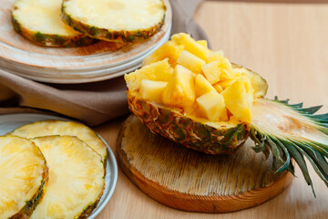 Chopped pineapple salad in half pineapple. Fresh delicious pineapple cut into pieces. Tasty summer pineapple sliced fruit dessert with ingredients on kitchen table in cooking process.