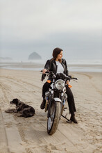 Trendy Woman Riding Motorcycle On Beach With Her Dog