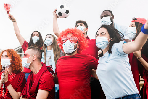 Multiracial group of friends wearing protective face mask screaming and watching soccer match at stadium during the coronavirus pandemic - New normal for live sports concept