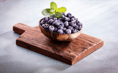 Bowl of fresh blueberries on rustic wooden board. Organic food blueberries and mint leaf for healthy lifestyle.