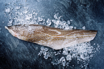 raw norwegian skrei cod fish filet with skin offered as top view with ice on a black board with copy