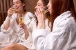 © alfa27 - young women in white bathrobe relaxing in spa salon, drinking champagne, celebrating holidays together. beauty, people concept. focus on redhead female taking sip
