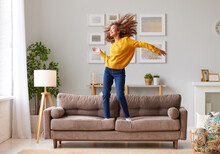 Happy African American Teen Girl Jumping On Sofa While Having Fun On Weekend At Home