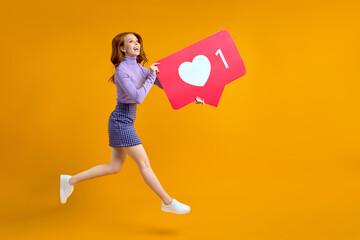 redhead female chasing likes and appreciation, jumping woman keeping social media heart icon looking copyspace isolated on yellow color background in studio