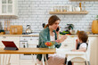 © Danil Nevsky/Stocksy - Mother feeding baby and talking on smartphone in kitchen