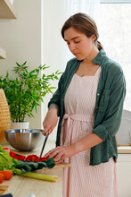 Focused Housewife Cutting Vegetables For Salad In Kitchen
