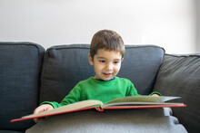 Kid  Reading A Book Sitting On The Sofa