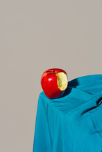 Nibbled Red Apple On A Blue Satin Fabric