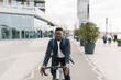 © Mihajlo Ckovric/Stocksy - Young african american businessman riding a bicycle to work in the urban city zone