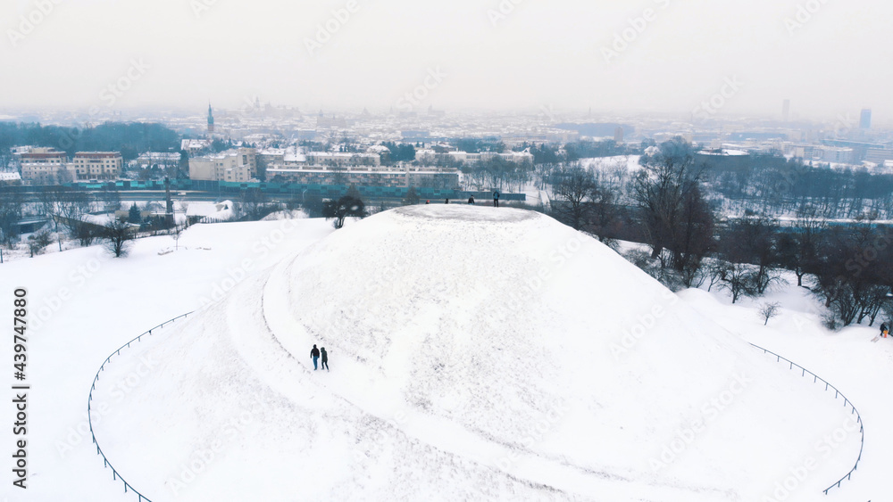 Panoramic view of the Krakus Mound (Kopiec Krakusa) also called Krak Mound. A tumulus located in the Podgórze district of Kraków, Poland. Tourists can be seen standing. Whole area covered with snow.  - obrazy, fototapety, plakaty 