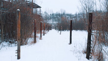 Closeup View Of Electric Fence Poles In The Liban Kamieniolom. The Place, Where The Movie The Schindler´s List Was Shot. Krakow, Poland. Grove Of Trees In The Background. Whole Area Covered With Snow.