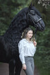 Happy young woman with the frisian horse in the summer forest.