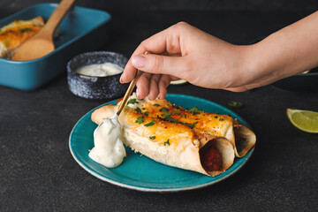 Woman putting sauce onto plate with tasty enchilada