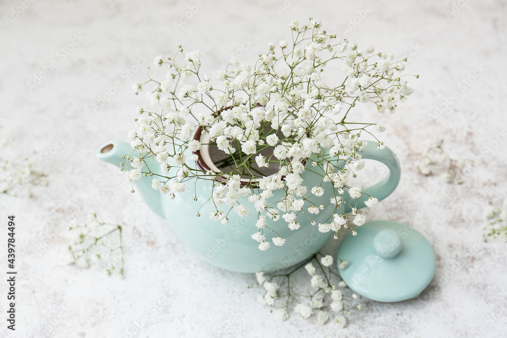 Teapot with beautiful gypsophila flowers on light background