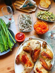 two halves of homemade fried chicken cooked in an aerogrill, homemade salads and herbs on a wooden table.