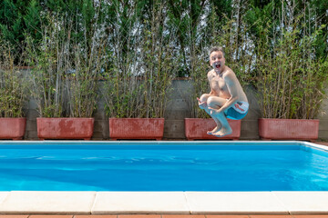 White man with a funny expression takes a cannon ball dive in a swimming pool on a sunny day