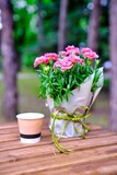 Fototapeta Nowy Jork - Many small pink cloves in vase on wooden table outdoor.