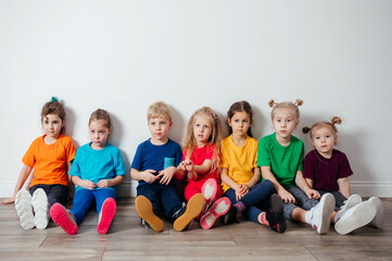 Wall Mural - Cheerful children sitting on a floor near the wall