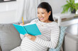 © Syda Productions - pregnancy, people and leisure concept - happy smiling pregnant asian woman sitting on sofa and writing to diary or notebook at home