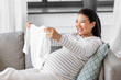 pregnancy, holidays and people concept - happy smiling pregnant asian woman with baby's bodysuit at home