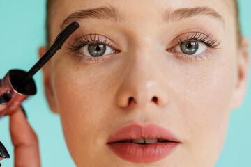 Young blonde woman applying mascara and looking at camera