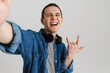 © Drobot Dean - Young brunette man with headphones smiling and gesturing horns sign
