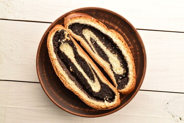 Two slices of freshly baked poppy seed roll, on a clay plate on a wooden table, close-up, top view.