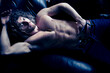 Portrait of attractive shirtless muscular man with beard and sixpack abs lying in leather armchair, looking at camera