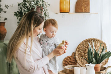 Wall Mural - mom young woman and her little girl daughter stands in the kitchen of a country house with duckling in hands and bathing in sink, summer vibes concept