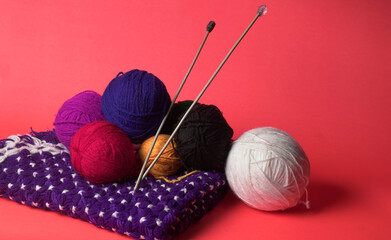 A Piece of knitting with color threads ball of yarn and a knitting needle on red background.