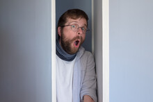 Bearded Man In Casual Clothes Is Hiding In A Closet, He Peeps Through The Open Door And Looks In Surprise With An Open Mouth And Big Eyes. 