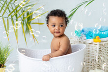 Smiling African Baby Bathes And Plays In The Bubble Bath At Home, A Concept Of Care And Hygiene For Young Children