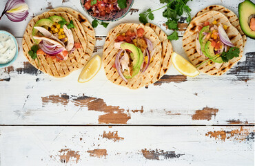 Mexican tacos with grilled chicken, avocado, corn kernels, tomato, onion, cilantro and salsa old white wooden table. Traditional Mexican and Latin american street food. Top view.