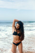 © verona_studio - Beautiful latin woman in black bikini on tropical beach. Portrait of happy young girl at sea. Brunette tanned girl in swimwear