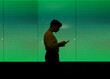 © Jimena Roquero/Stocksy - Young non-binary person standing in front of green lighted screen with smartphone
