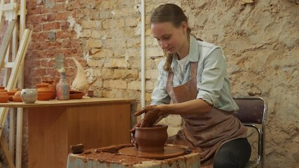 Wall Mural - Female potter sculpts a clay pot. The sculptor works with clay on a potter's wheel and at a table