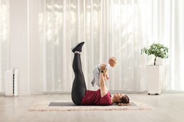 Canvas Print - Mother laying on an exercise mat and lifting a baby at home in a living room