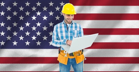 Wall Mural - Composition of smiling male construction worker using laptop over american flag