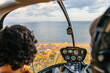 © Marcos Osorio/Stocksy - Passenger and pilot inside a helicopter while flying over the coast at sunset
