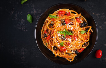 Spaghetti alla puttanesca - italian pasta dish with tomatoes, black olives, capers, anchovies and basil. Top view, flat lay