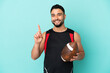 © luismolinero - Young arab man playing rugby isolated on blue background showing and lifting a finger in sign of the best