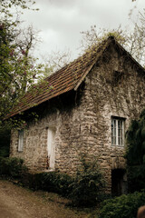 Poster - Vertical shot of an old stone house surrounded by green trees and plants under a gloomy sky