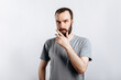 © Daria Lukoiko - Serious puzzled handsome male model with beard holding hand on chin as if thinking about something, squinting at camera with suspicious look and standing over gray background. Man decides what to buy