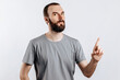 © Daria Lukoiko - Portrait of cheerful young handsome man smiling looking at camera pointing finger upwards on white background with space for advertising mock up