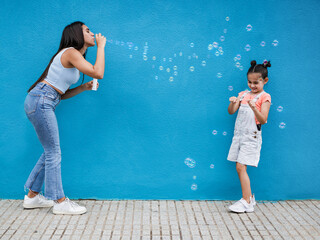 Wall Mural - Teenage girl blowing soap bubble to little sister - Sisters having playful time in the city