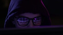 Portrait Of Female Hacker Wearing Eyeglasses Breaking Data Servers, Running A Virus In System, Working On Computer For Cyber Attack. Green Binary Hacking Code Reflecting In Eyeglasses In Dark Room.